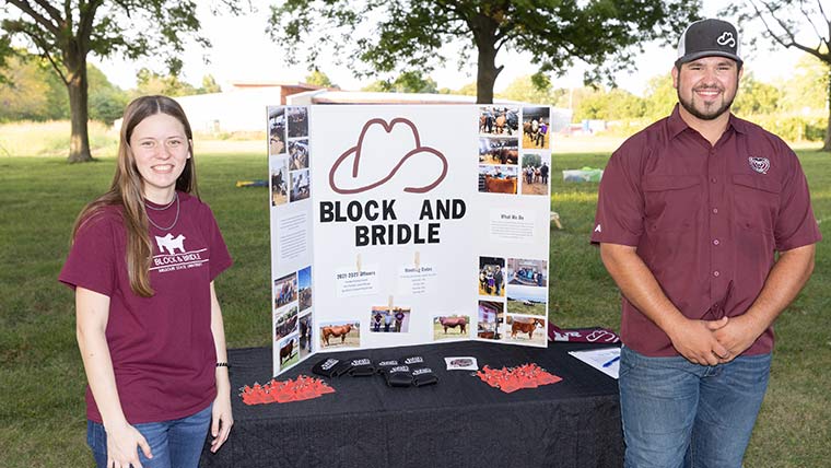 Two students standing in front of a poster for the Block and Bridle Club.