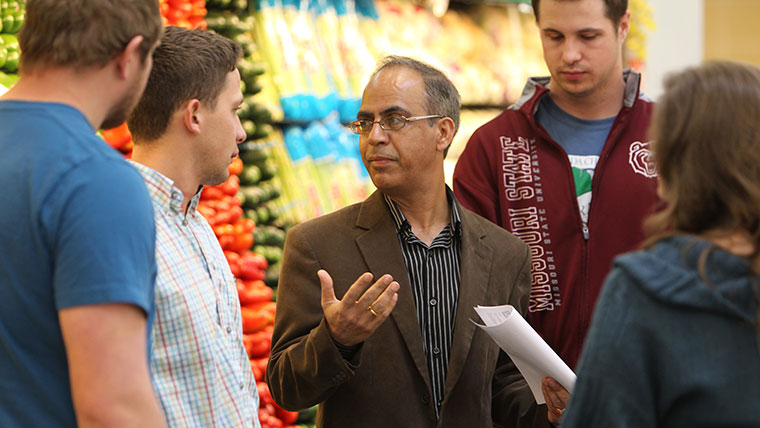 Dr. Arbindra Rimal leads a discussion with a group of students in front of a produce display.