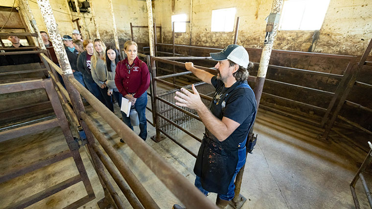 An agriculture worker takes students and faculty on a tour of a slaughterhouse.