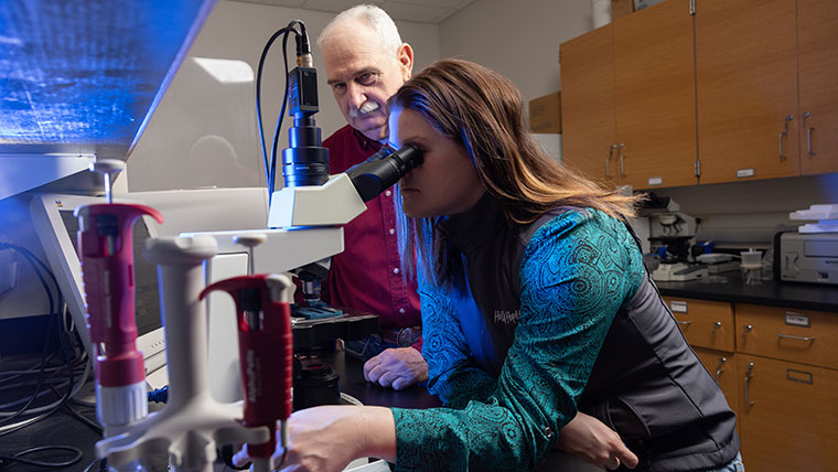 An agriculture student peers through a telescope. Dr. Gary Webb stands to the side to supervise.