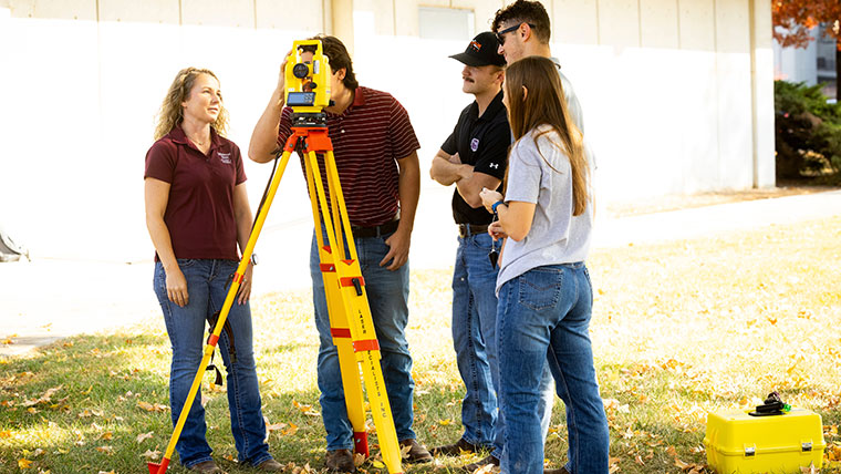 A professor demonstrates how to use a surveying tripod to his students.