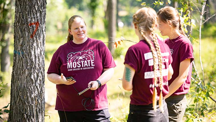 Dr. Melissa Bledsoe, dean of the Darr College of Agriculture, talks to two students during a research project in the woods.