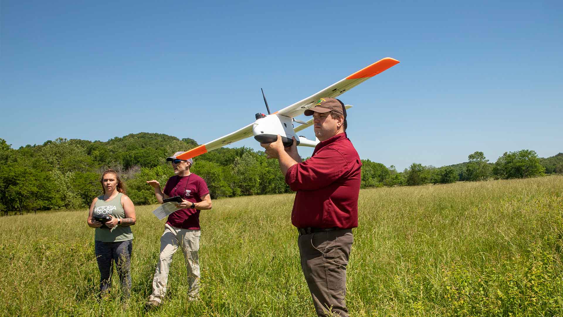 Two professors and a graduate student get ready to fly a drone in a prairie for a land survey.