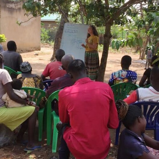 Grace Ford giving a presentation to a group of villagers during a study abroad experience in Africa.