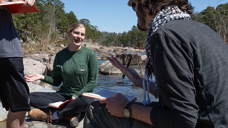 Two students have a conversation while conducting research along a riverbed in the Ozarks.