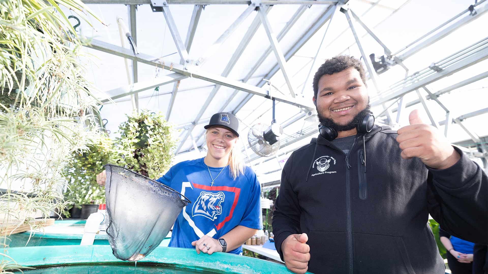 Two Missouri State-West Plains students smile for the camera while working in a greenhouse on campus.