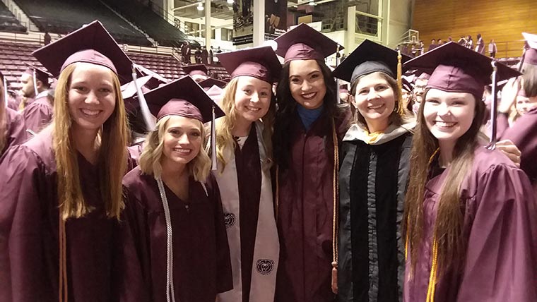 Animal science students in cap and gown with professor at commencement ceremony.